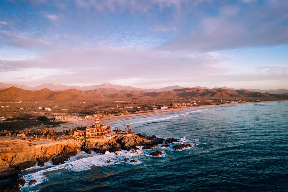 A coastal landscape with a rocky shoreline, a beach, and mountains in the background.