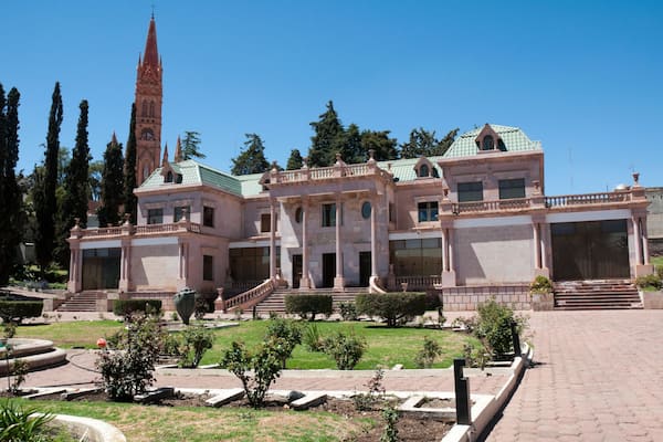 A historic building with a prominent tower, a well-manicured garden, and a grand entrance.