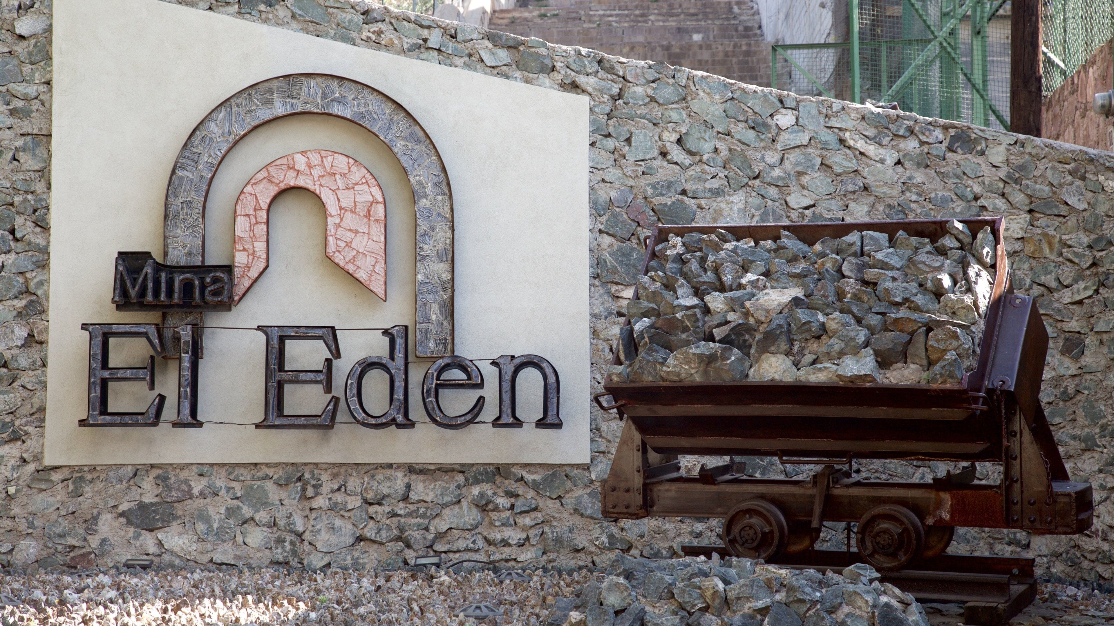 Señalización para 'Mina El Eden' con un muro de piedra y un camión volquete lleno de rocas.