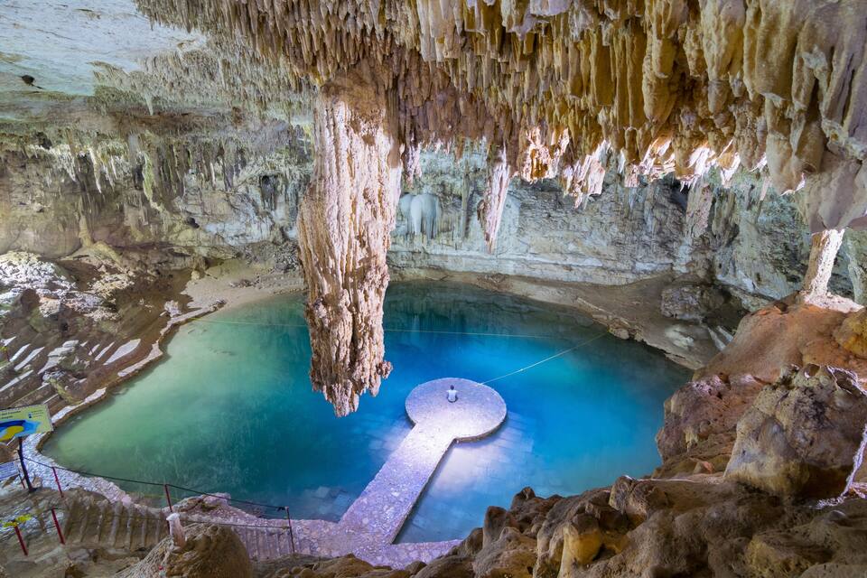 Una grotta con stalattiti, una grande vasca circolare e una formazione rocciosa a forma di chiave.