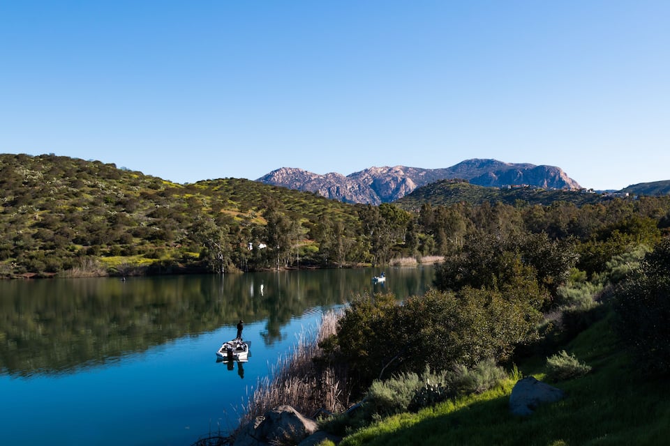Un lago tranquilo con un bote, rodeado de exuberante vegetación y montañas al fondo.
