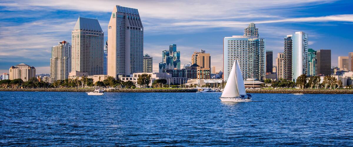 A city skyline with tall buildings and a sailboat on the water.
