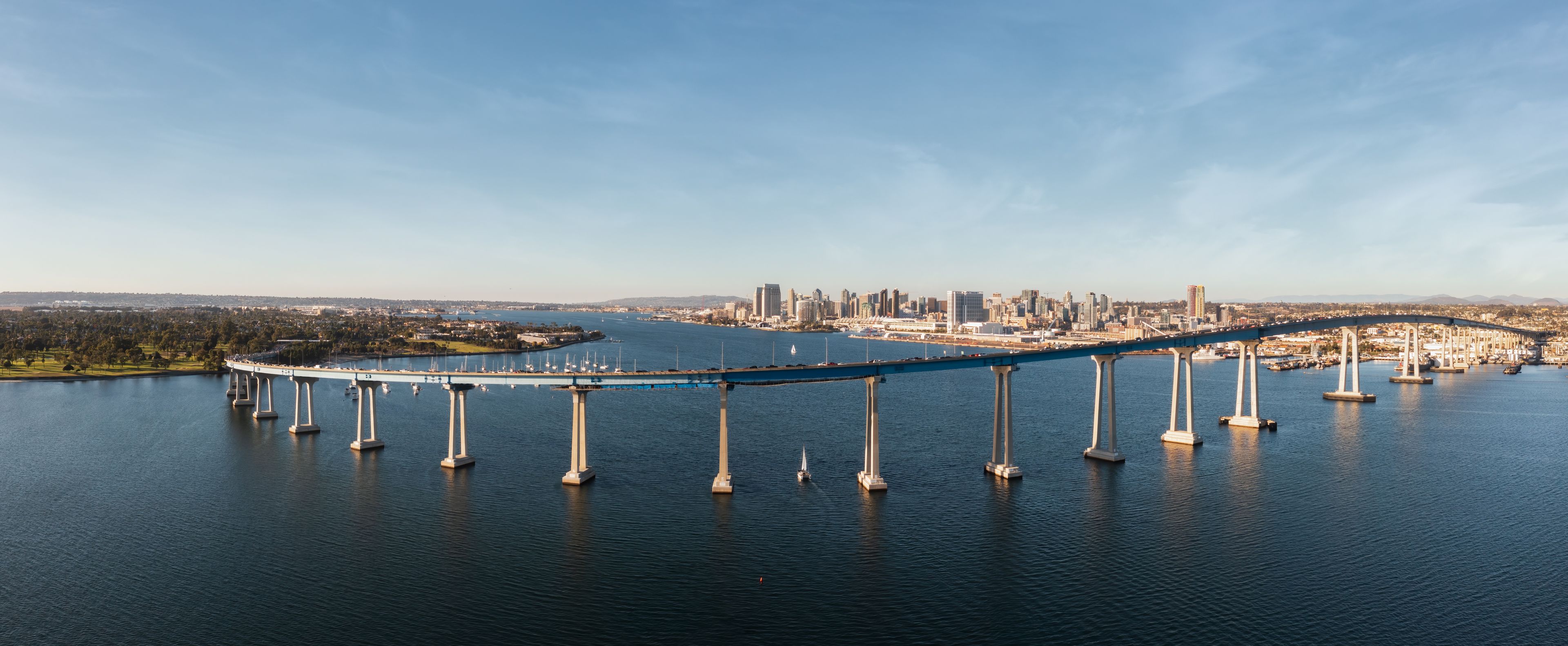 A large suspension bridge over a body of water with a city skyline in the background.
