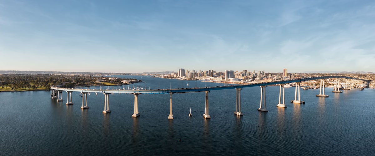 A large suspension bridge over a body of water with a city skyline in the background.