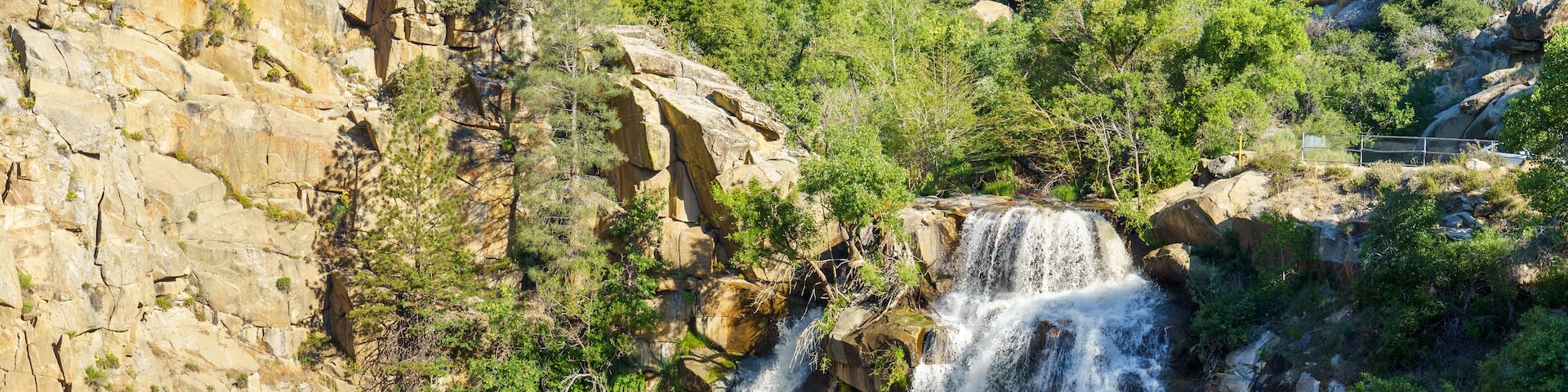 Una cascada se precipita por un acantilado rocoso, rodeada de vegetación.