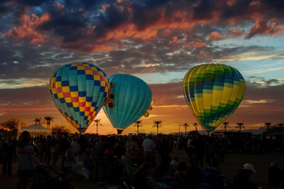Trois ballons à air chaud aux couleurs vives, se détachant sur le ciel au coucher du soleil.
