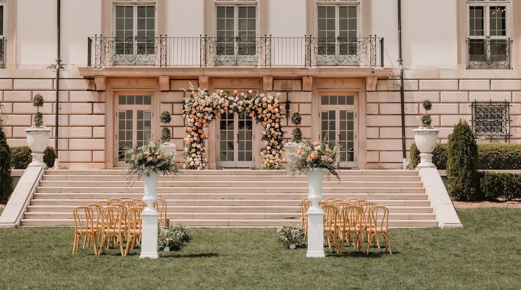 Elegant outdoor wedding setup with floral arch in front of a mansion
