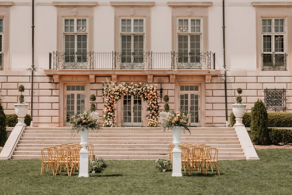 Un edificio imponente con una escalera que lleva a un balcón, decorado con motivos florales y sillas blancas.