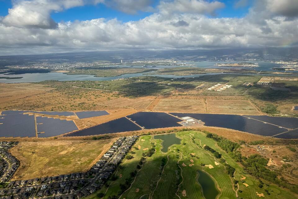 An aerial view of a coastal city with a marina, residential areas, and agricultural fields.