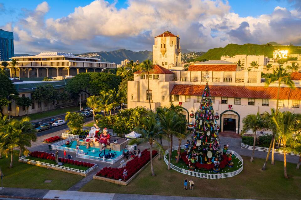 Un grand bâtiment doté d’une tour, de palmiers et d’un sapin de Noël décoré.