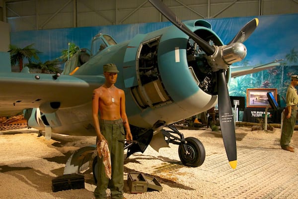 A vintage military aircraft on display with a mannequin in uniform standing in front.