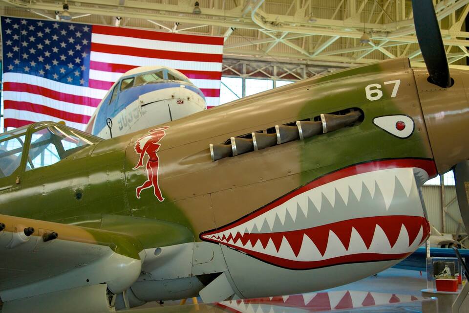 Un avió militar amb el morro decorat amb una boca de tauró, número 67, dins d'un hangar amb banderes dels Estats Units.