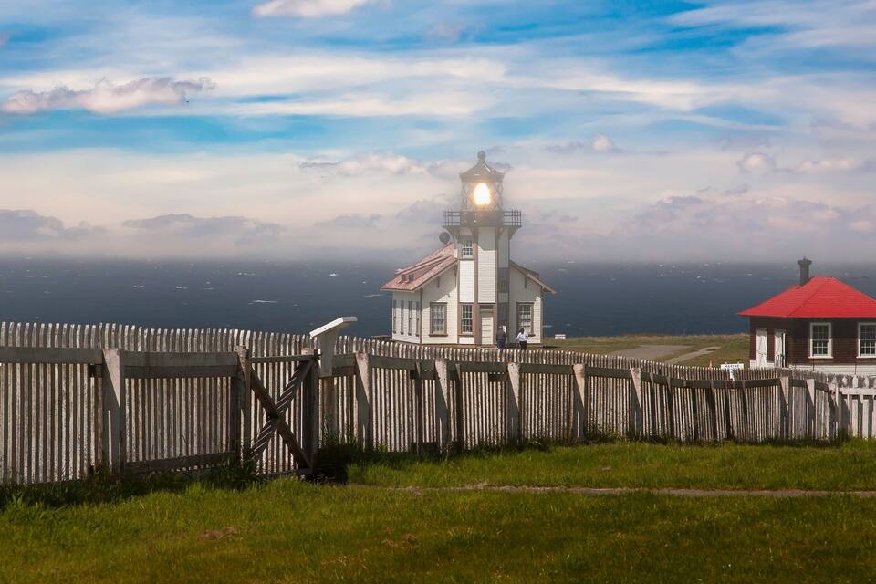 Un faro con techo rojo, cerca hay una valla de madera y un área con césped.