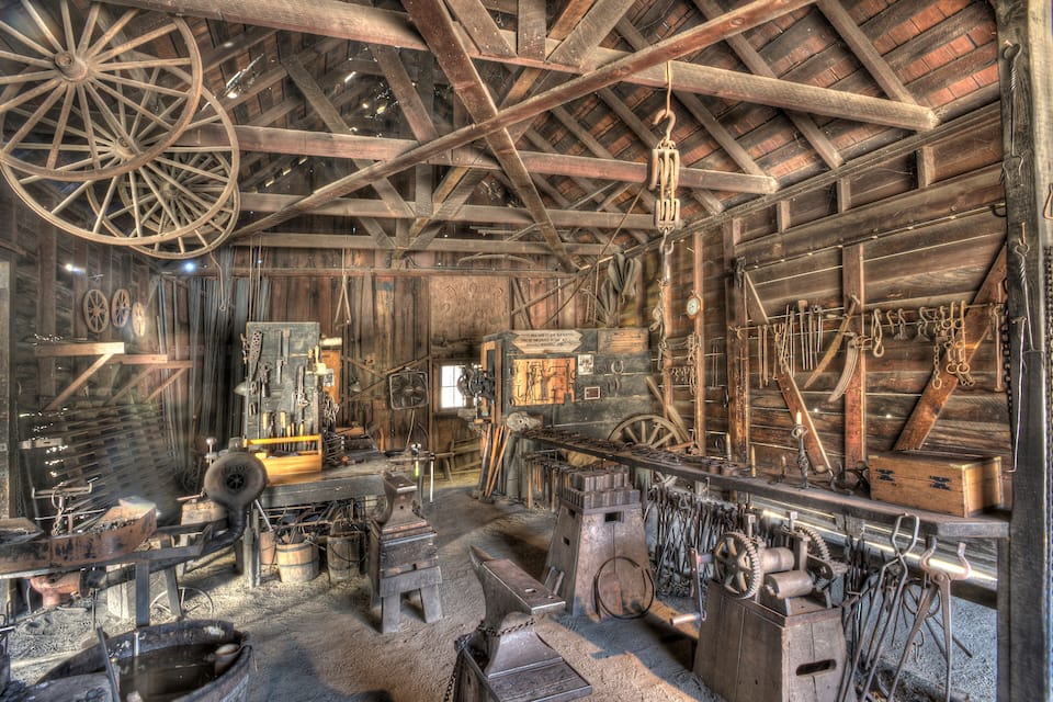 Une forge à l’ancienne, avec des poutres en bois, des enclumes et divers outils.
