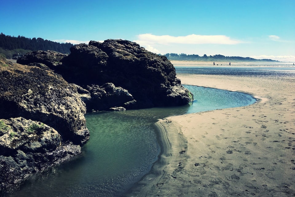 A beach with clear water, large rocks, and a distant shoreline.