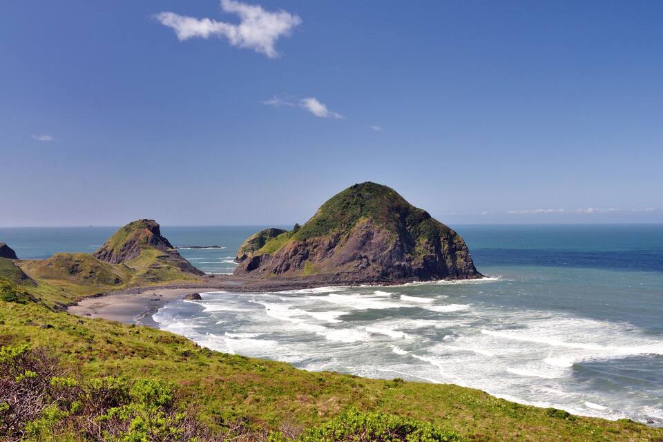 A coastal landscape with green hills and rocky outcrops.
