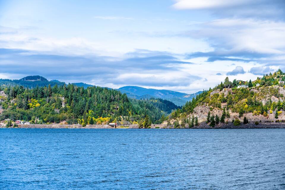 A coastal landscape with a body of water, green hills, and a small bridge.