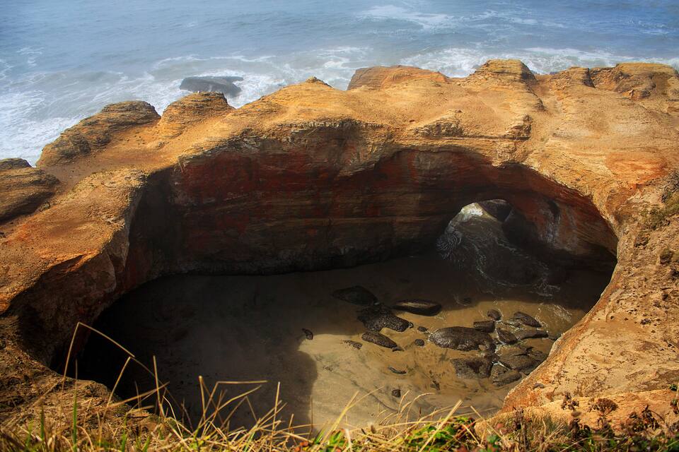 A coastal rock formation with a cave-like opening and a small pool of water.