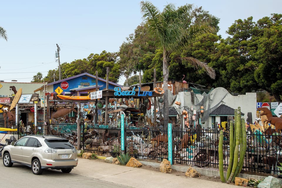 Un espace clos où l’on peut voir des cactus, un bâtiment bleu avec une enseigne et une voiture garée dans la rue.
