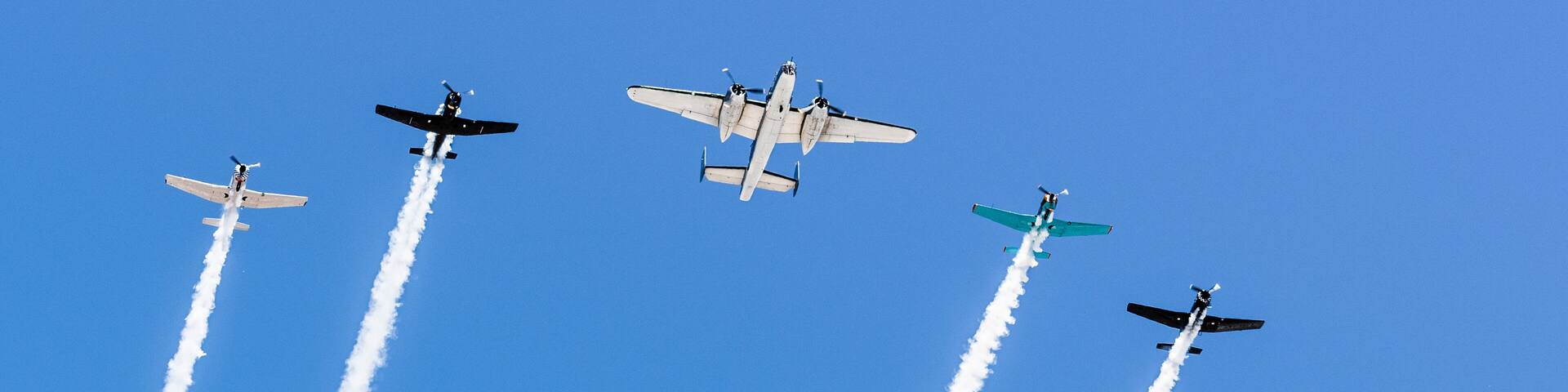 Historical airplanes flying in formation, leaving behind a white smoke trail; California