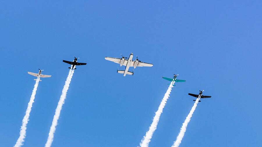 Historical airplanes flying in formation, leaving behind a white smoke trail; California