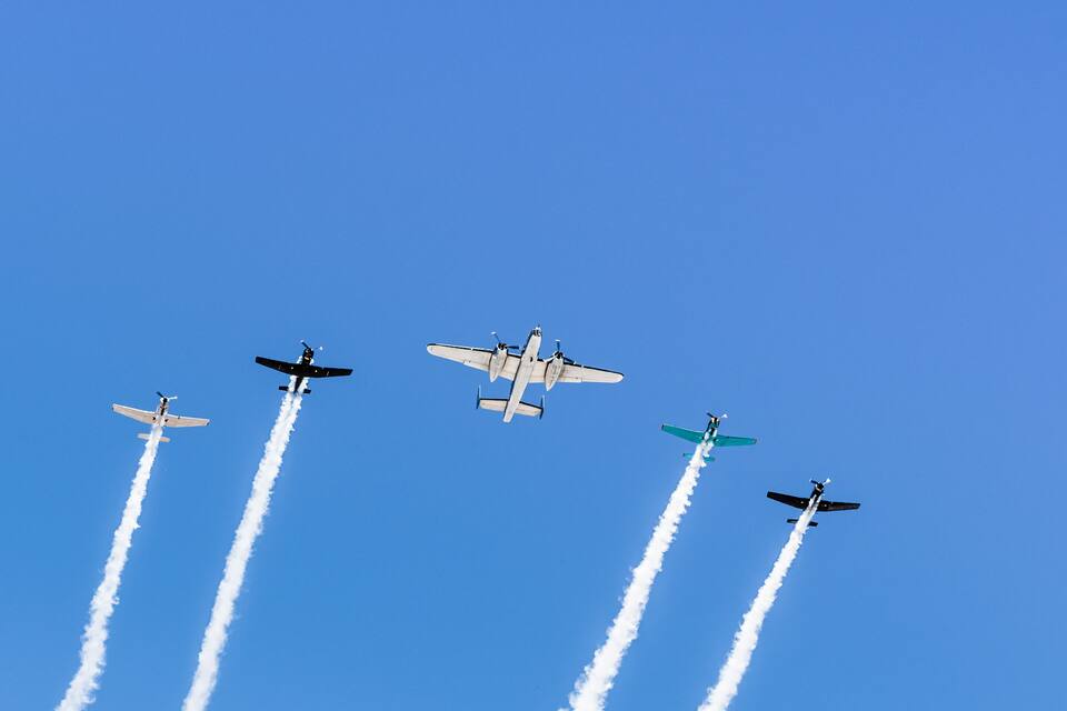 Cuatro aviones volando en formación, dejando estelas de humo contra un cielo azul despejado.