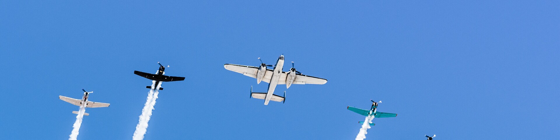 Historical airplanes flying in formation, leaving behind a white smoke trail; California