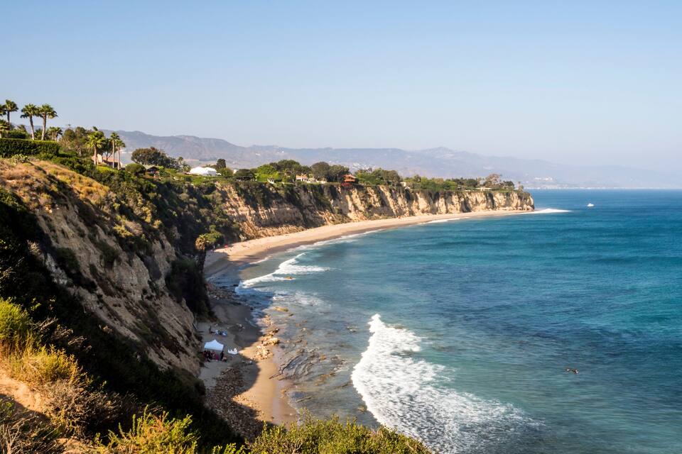 Paisatge costaner amb una platja sorrenca, penya-segades rocoses i oceà blau clar.