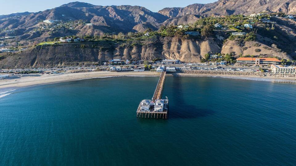 Un muelle se adentra en una bahía tranquila, con montañas al fondo.
