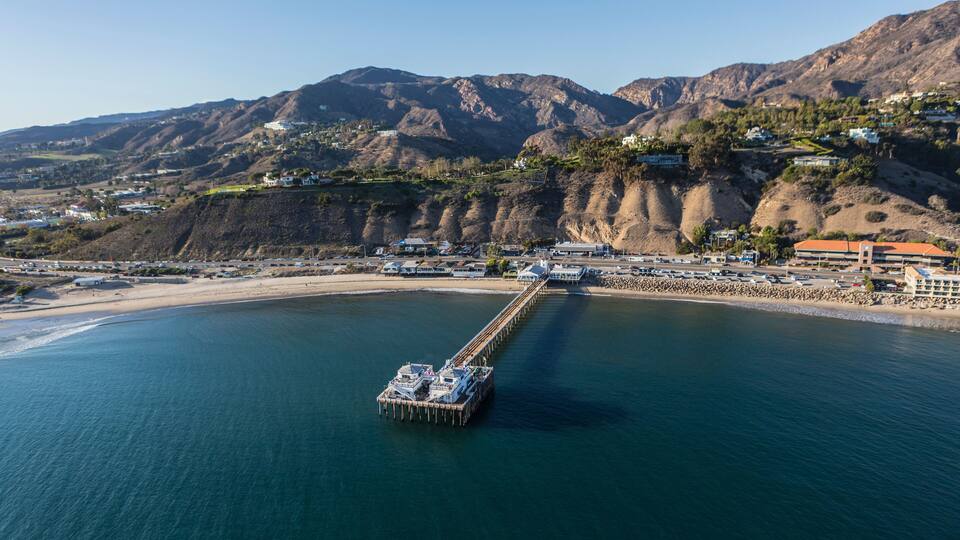 Un muelle se adentra en una bahía tranquila con montañas al fondo.