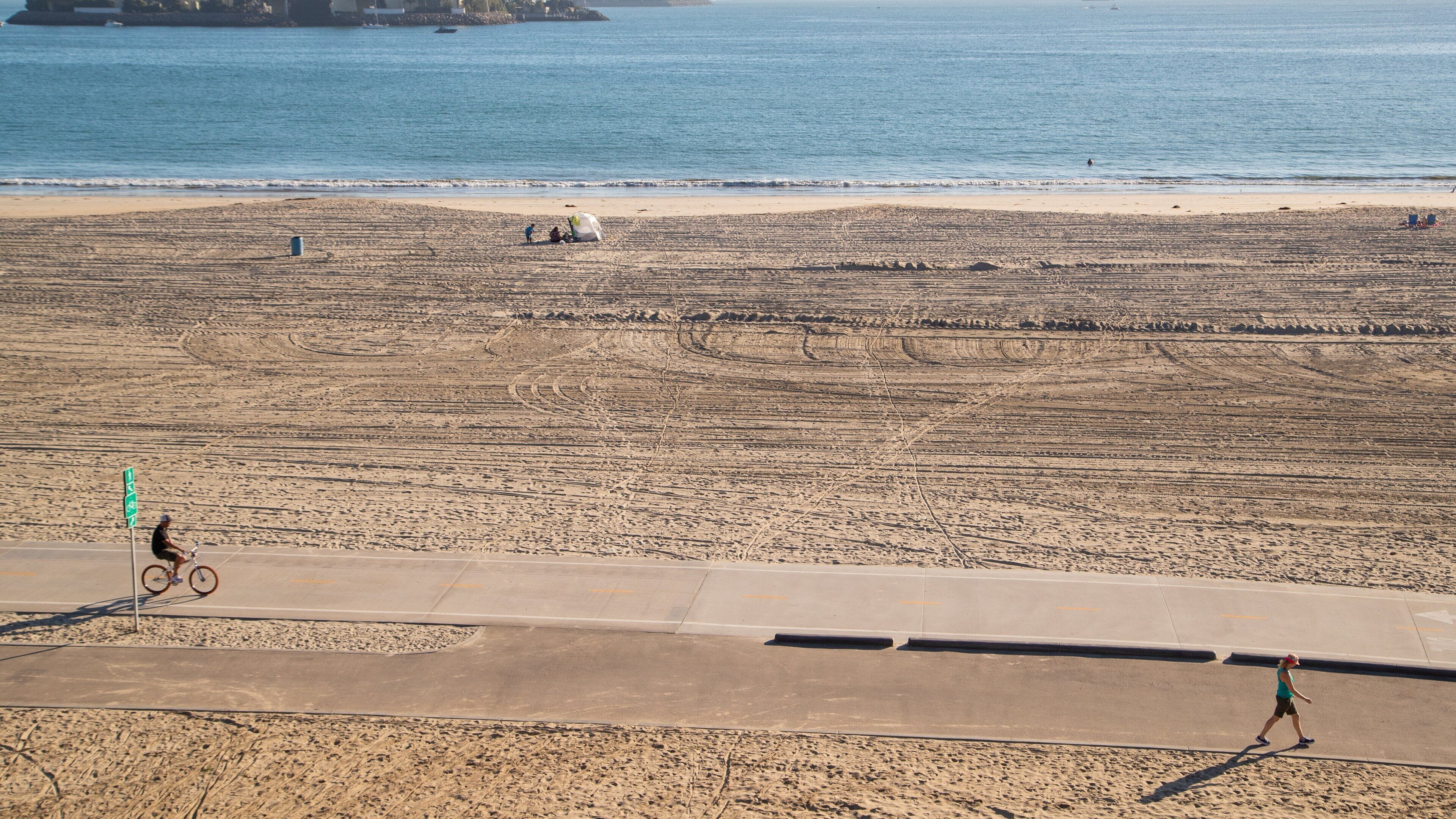 A beach with a cyclist and a pedestrian.