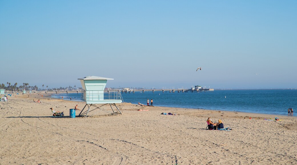 A beach with a lifeguard tower, people sunbathing, and a pier in the background.