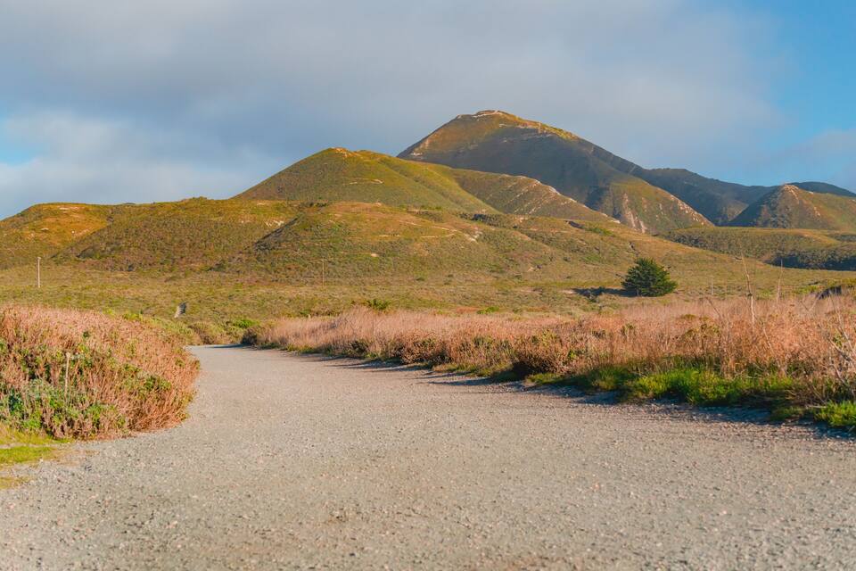 A gravel road winding through a hilly landscape with sparse vegetation and distant mountains.
