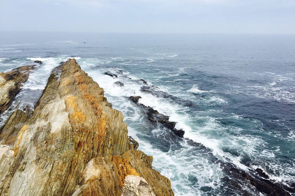 A rugged coastline with a prominent cliff and turbulent sea waves.