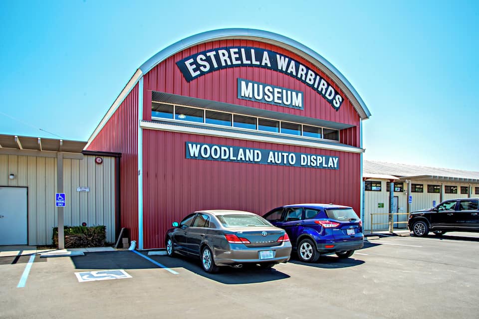 The Estrella Warbirds Museum building with a red exterior and a sign for the Woodland Auto Display.