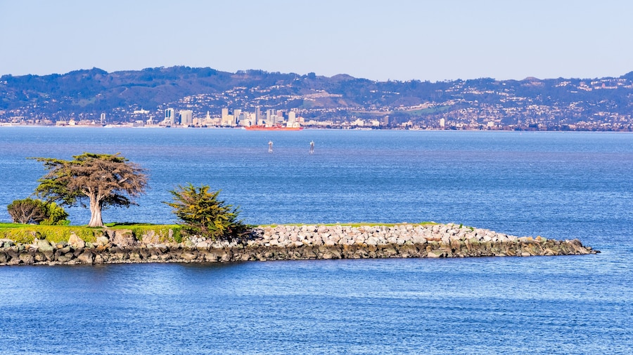 Point San Bruno Park jetty on the shoreline of San Francisco Bay; Port of Oakland, Oakland city skyline and residential neighborhoods built on the hills of East Bay visible in the background