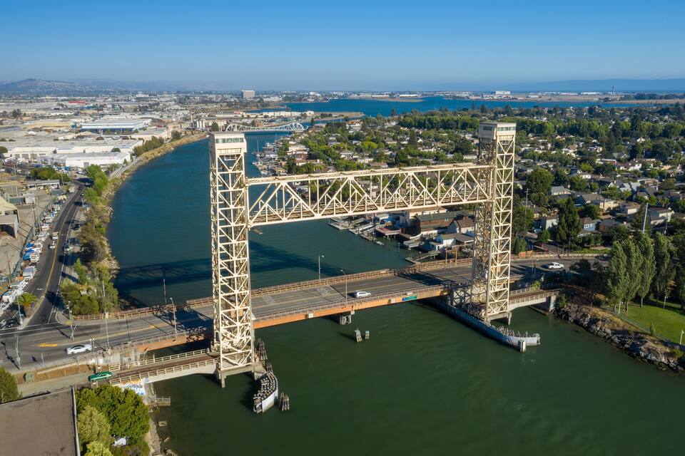 Uma grande ponte de aço que atravessa um rio, com uma cidade e área industrial ao fundo.