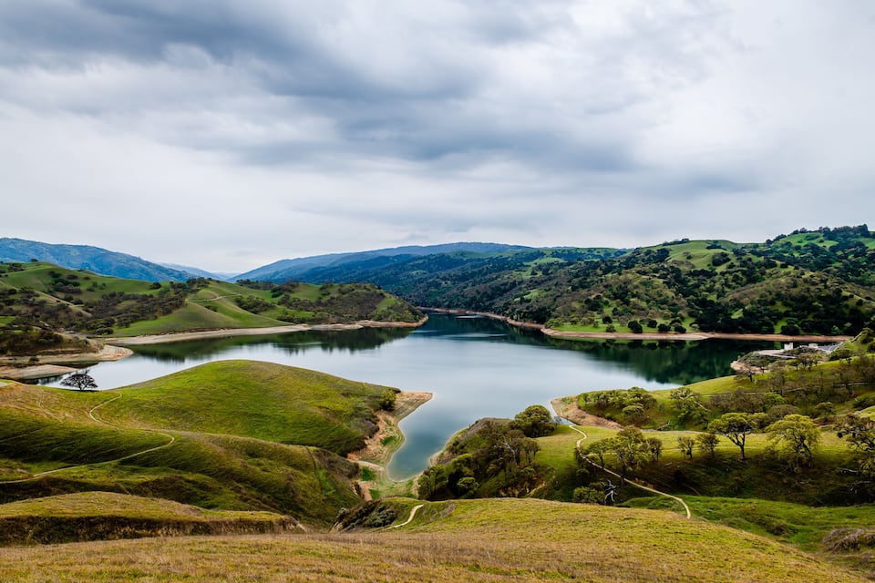 A serene valley with a calm lake surrounded by rolling hills and dense greenery.