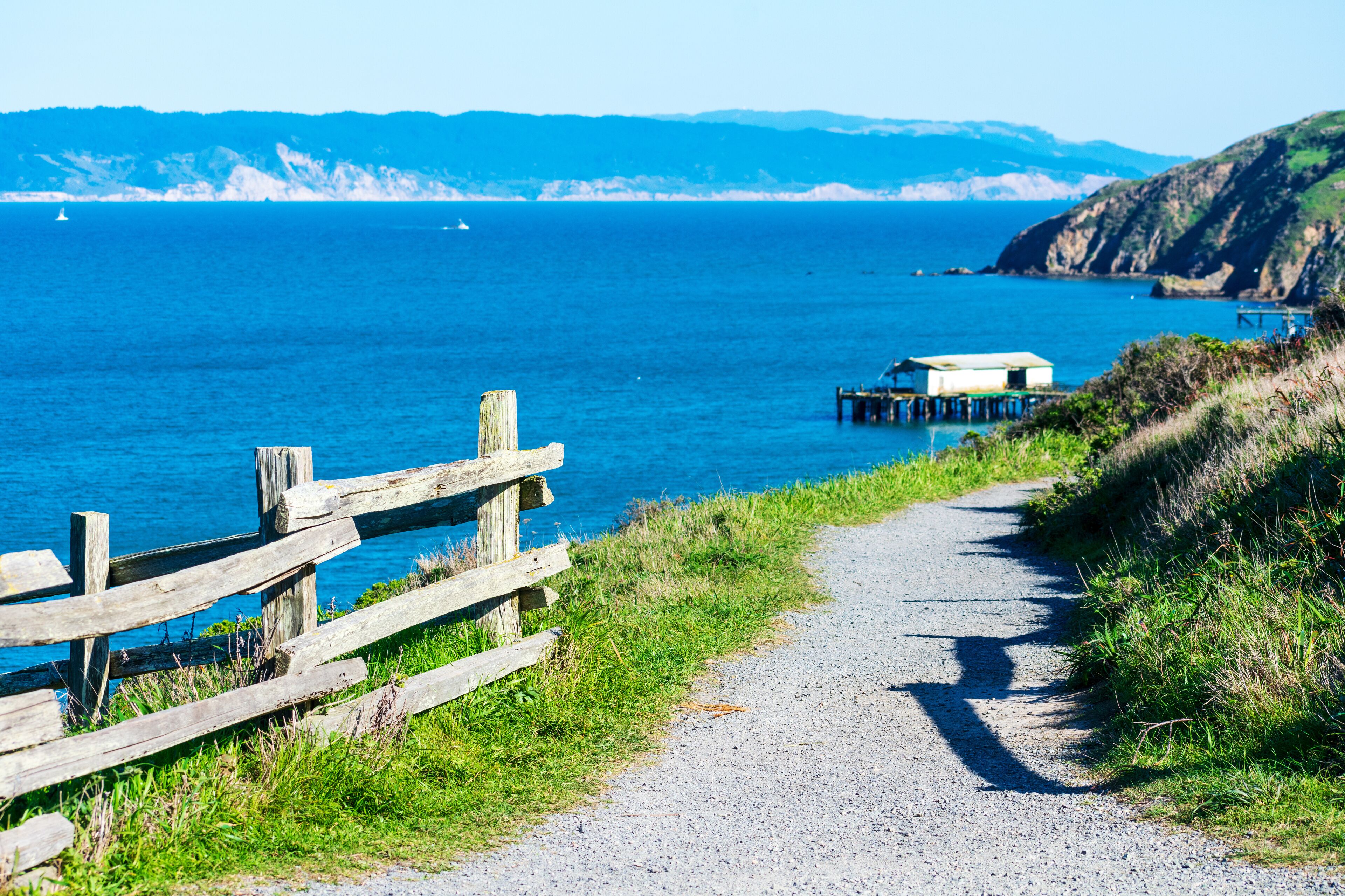 Unpaved hiking trail on cliff edge leading to lifeboat station at at Point Reyes Headlands. Scenic view of Drakes Bay calm blue water and coastline with white sandstone cliffs on horizon