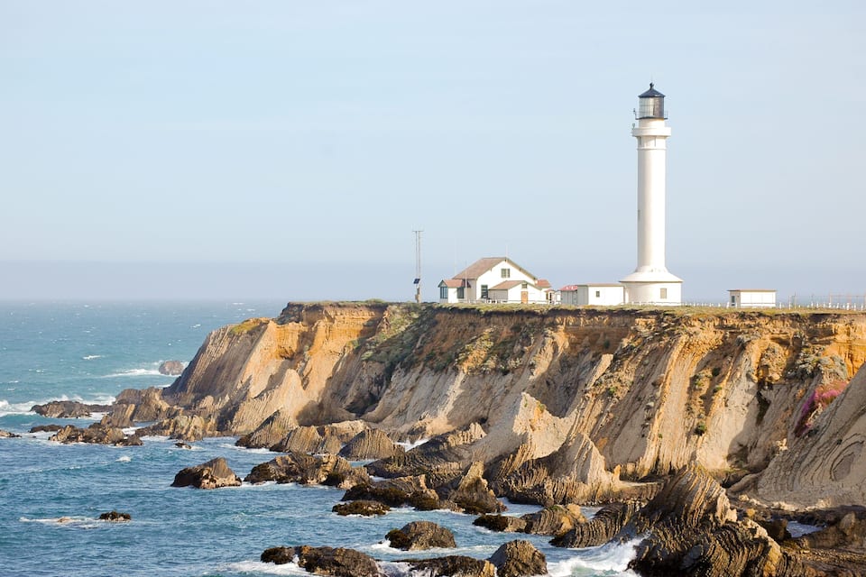 A lighthouse on a cliff by the sea, with a house nearby.