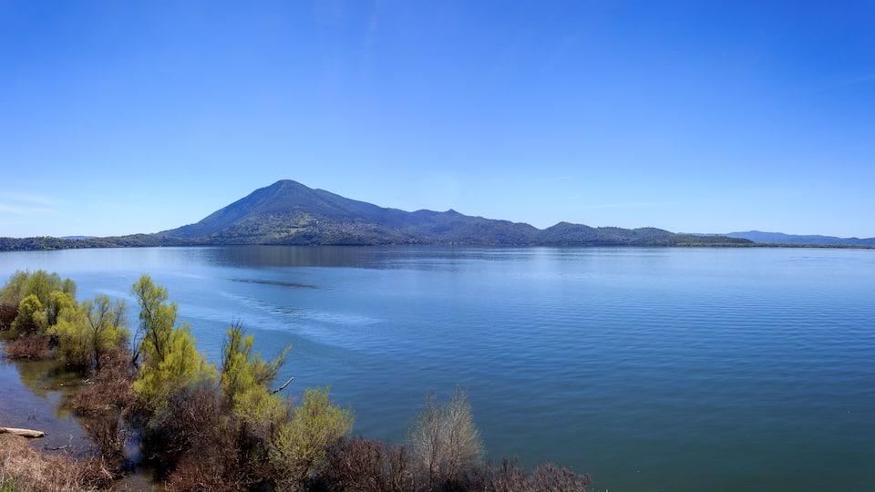 A calm lake with a mountain in the background and some trees in the foreground.