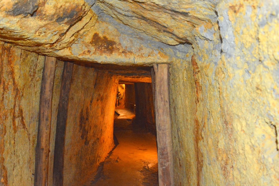 A narrow, dimly lit tunnel with rough, uneven walls and a wooden floor.