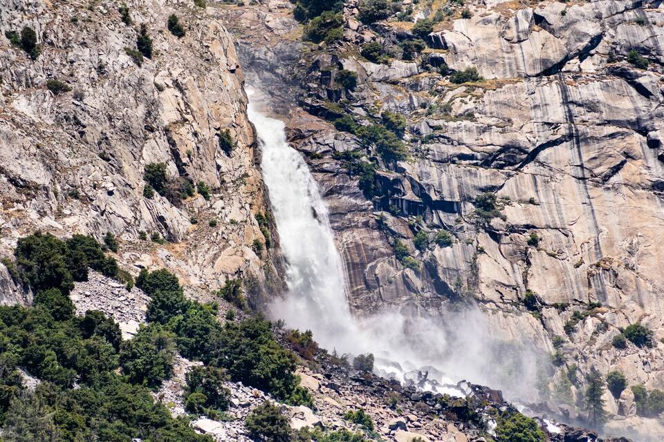 Uma cascata desce por um penhasco rochoso, cercada por vegetação rala.