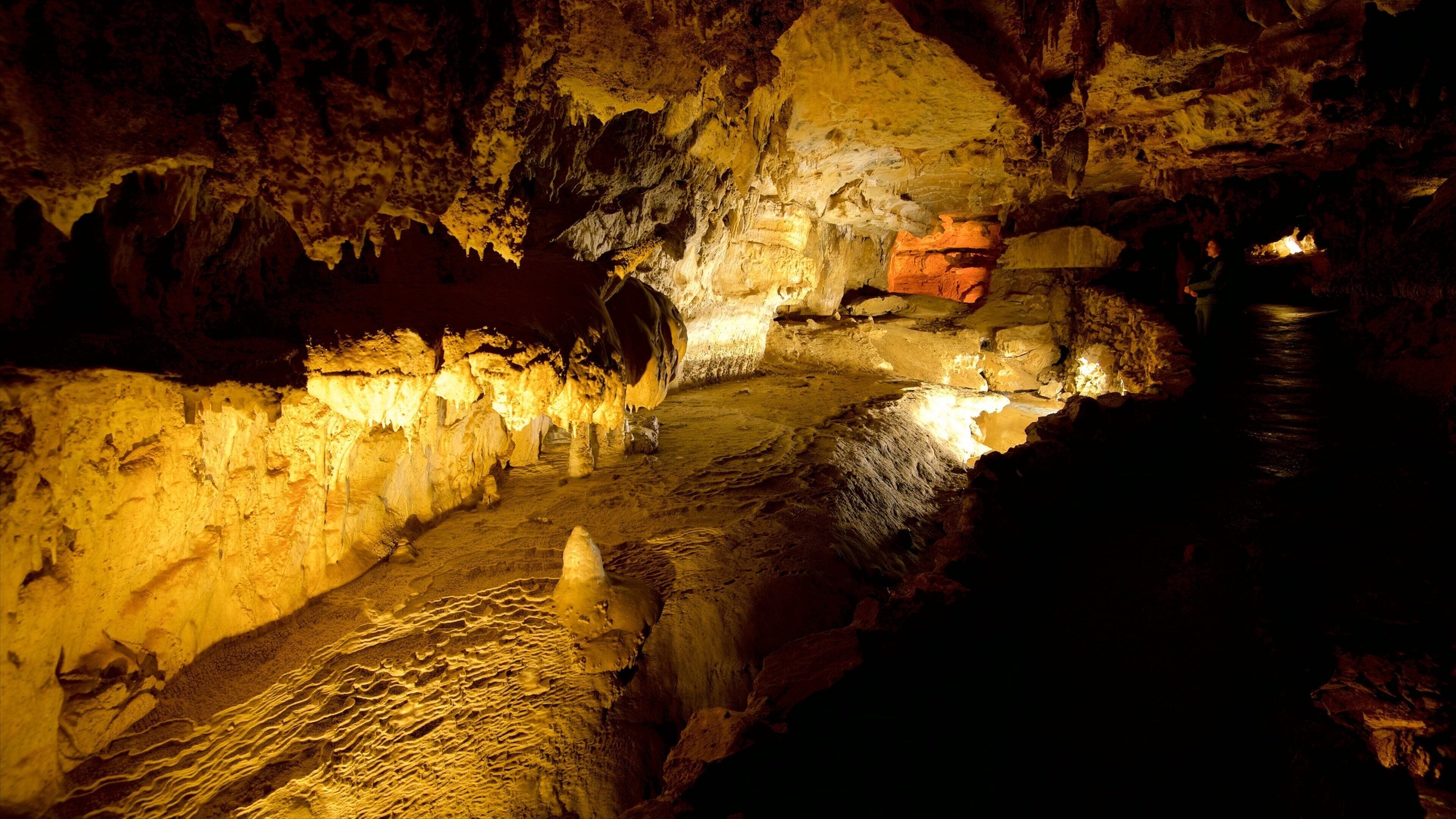 Eine Höhle mit Stalaktiten und Stalagmiten, einem Feuer und einer Person in der Nähe des Eingangs.
