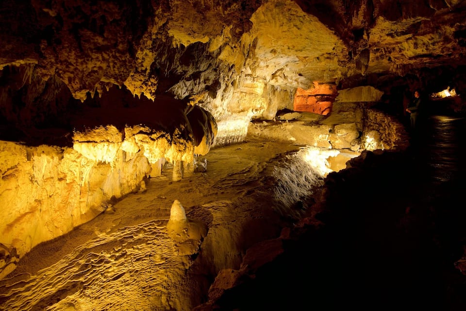 Eine Höhle mit Stalaktiten und Stalagmiten, einem Feuer und einer Person in der Nähe des Eingangs.