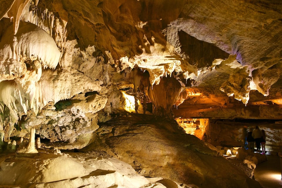 A cave with stalactites and stalagmites, dim lighting, and a few visitors.