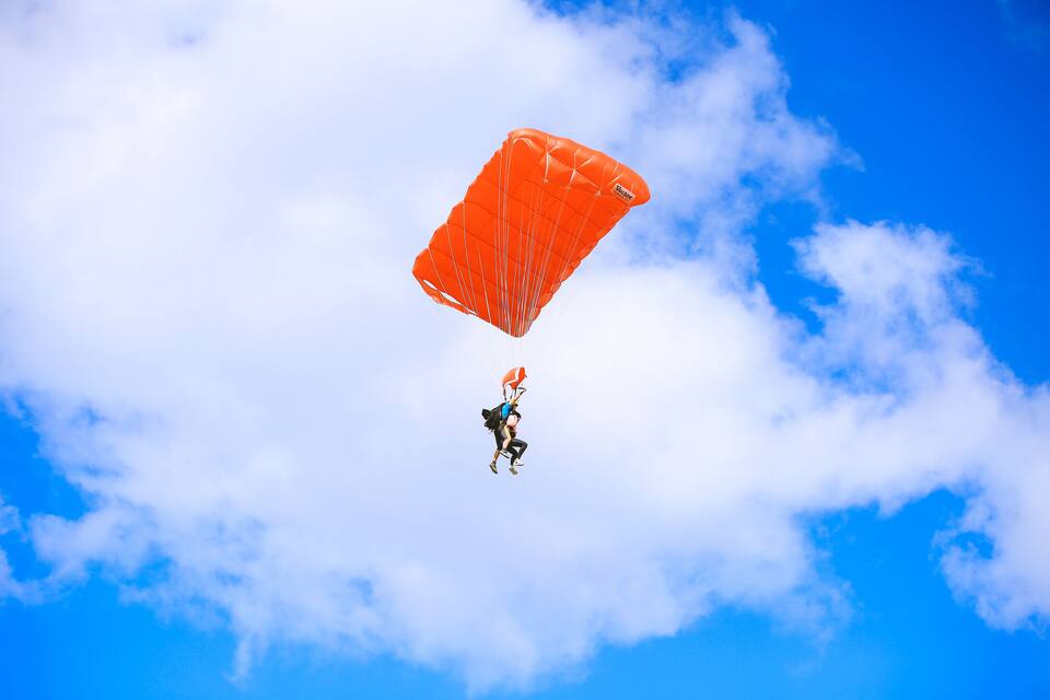 A person skydiving with an orange parachute against a blue sky with clouds.