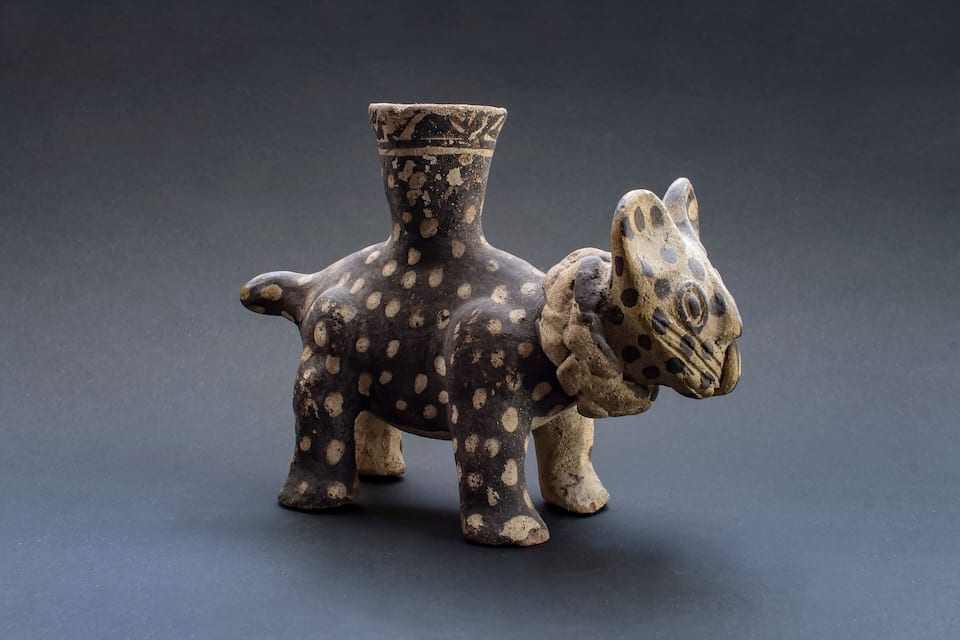 A small, dark-colored ceramic sculpture of a horse with a rider, featuring a simple design with white spots.
