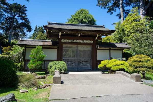 Ein traditionelles japanisches Tor mit einem Strohdach, umgeben von gepflegter Bepflanzung und Steinlaternen.