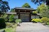 Ein traditionelles japanisches Tor mit einem Strohdach, umgeben von gepflegter Bepflanzung und Steinlaternen.